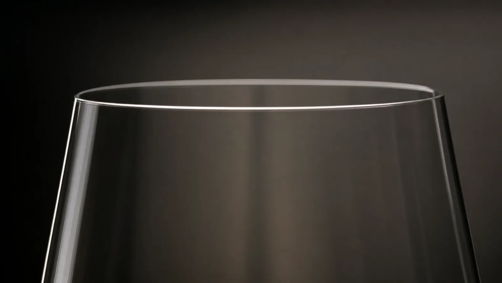 Close-up of the paper-thin rim of a crystal wine glass, backlit so the fragile edge glows against a dark background